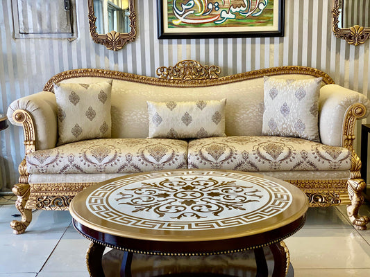 Decorative sofa with ornate gold frame and matching round table in a room with striped wallpaper.